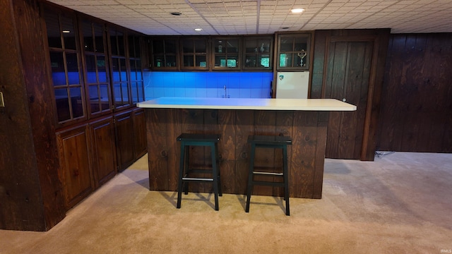 bar featuring dark brown cabinetry, sink, light carpet, and fridge