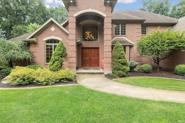 view of front of home with brick siding, a front lawn, and a shingled roof