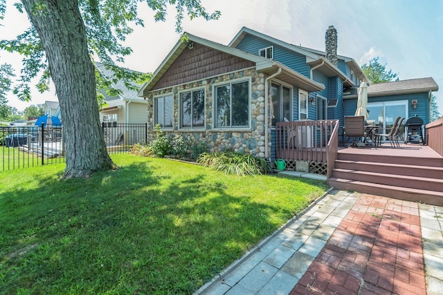 back of property with stone siding, a chimney, a yard, fence, and a wooden deck