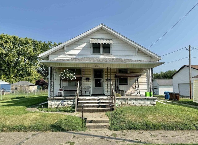 bungalow-style house featuring a porch, a garage, an outbuilding, and a front yard