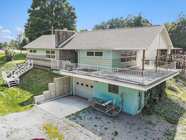 rear view of house featuring a chimney, driveway, a shingled roof, and an attached garage