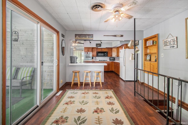 kitchen with brown cabinets, freestanding refrigerator, a peninsula, black microwave, and ceiling fan