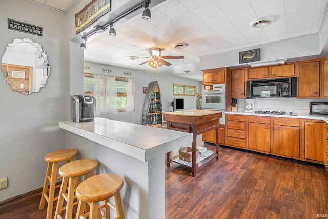 kitchen featuring dark wood-type flooring, black microwave, light countertops, brown cabinetry, and gas cooktop