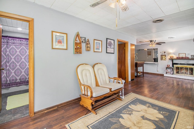 sitting room featuring a glass covered fireplace, baseboards, ceiling fan, and wood finished floors