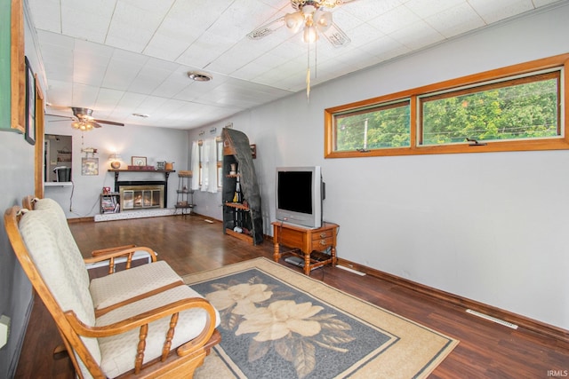 living area with baseboards, wood finished floors, a glass covered fireplace, and a ceiling fan