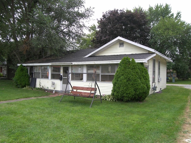 view of front of house with a sunroom, roof with shingles, and a front lawn