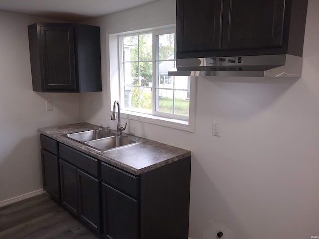 kitchen with wall chimney range hood, sink, and dark wood-type flooring