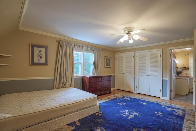 bedroom with ornamental molding, wood-type flooring, multiple closets, and ceiling fan