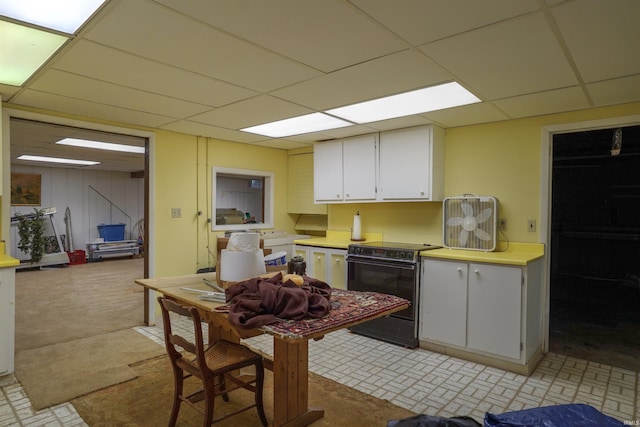 kitchen featuring light colored carpet, black / electric stove, a drop ceiling, and white cabinets