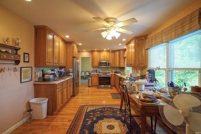 kitchen featuring light wood-type flooring, backsplash, ceiling fan, and appliances with stainless steel finishes