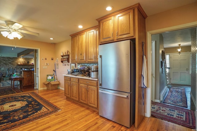 kitchen with light wood-type flooring, stainless steel fridge, decorative backsplash, and ceiling fan