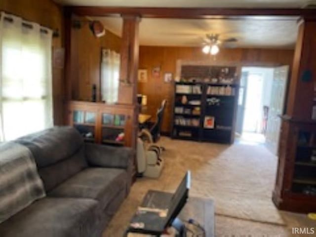 living room featuring wood walls, light colored carpet, ornate columns, and ceiling fan