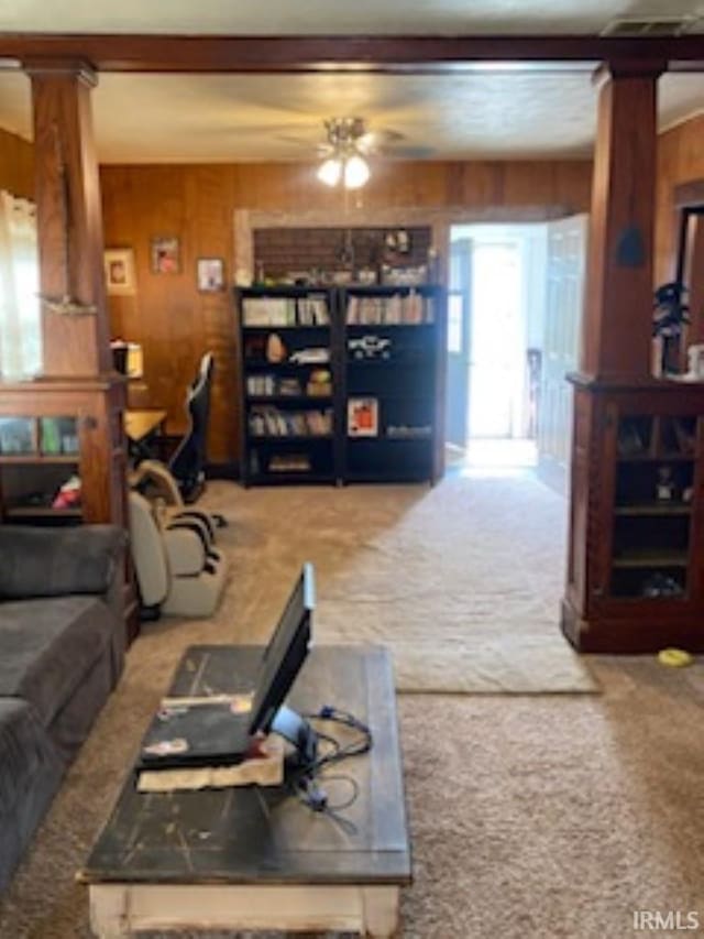 carpeted living room with wooden walls, ornate columns, and ceiling fan