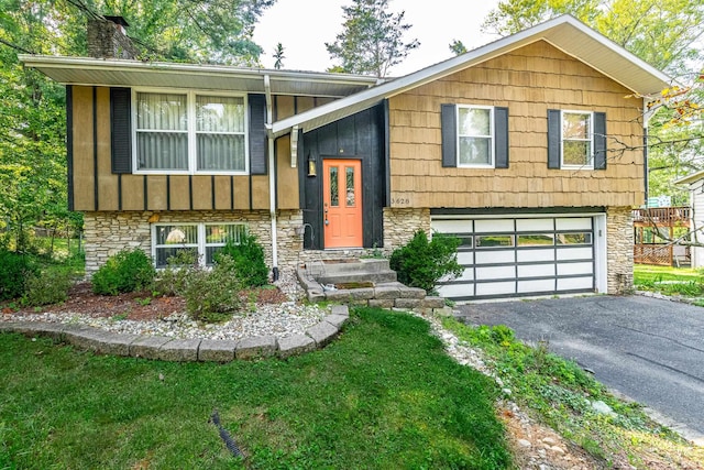 split foyer home featuring a chimney, a garage, stone siding, aphalt driveway, and board and batten siding