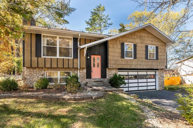 split foyer home with board and batten siding, a garage, stone siding, and driveway