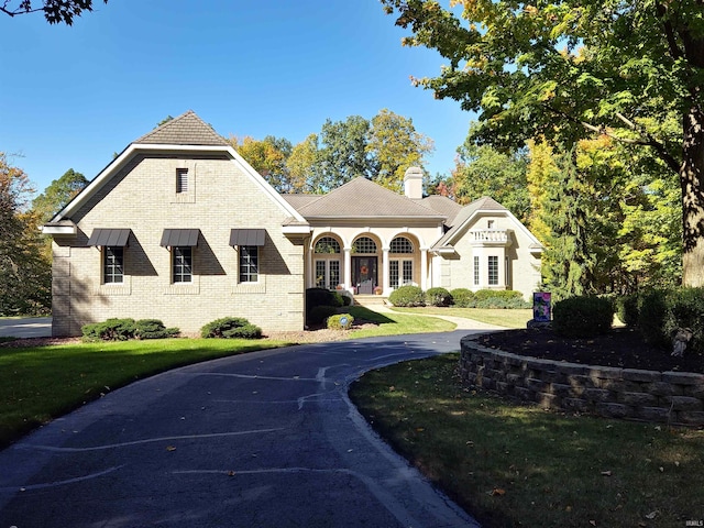 view of front of house with brick siding, a chimney, and a front lawn