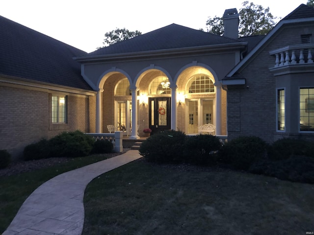 view of front of house featuring a porch, a chimney, and brick siding