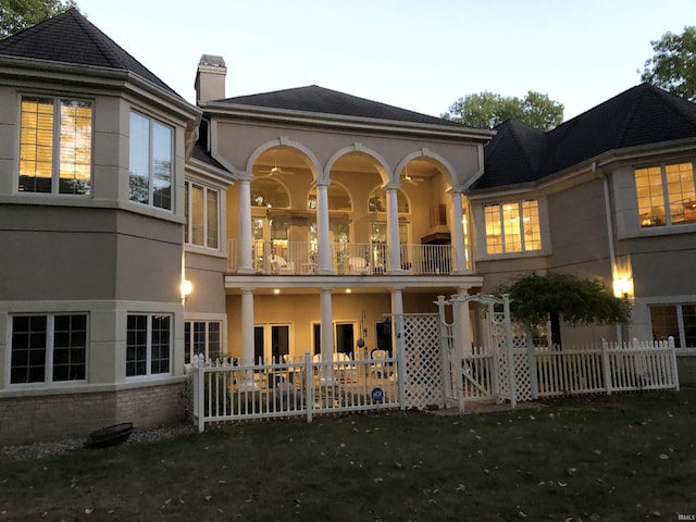 back of property with a balcony, a chimney, fence, and stucco siding