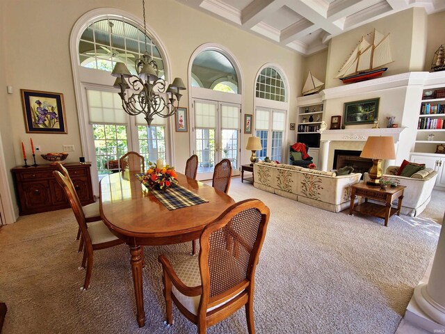 dining area featuring french doors, light colored carpet, a towering ceiling, an inviting chandelier, and coffered ceiling