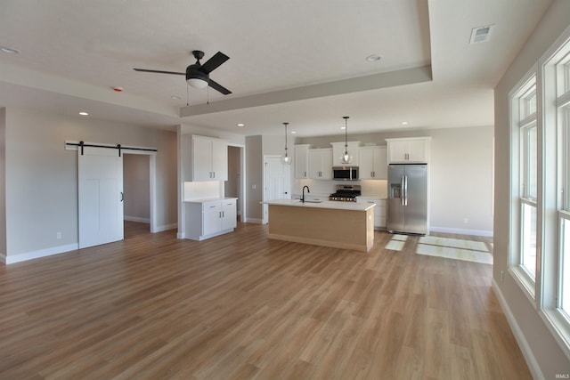 unfurnished living room with ceiling fan, sink, a barn door, light hardwood / wood-style floors, and a tray ceiling