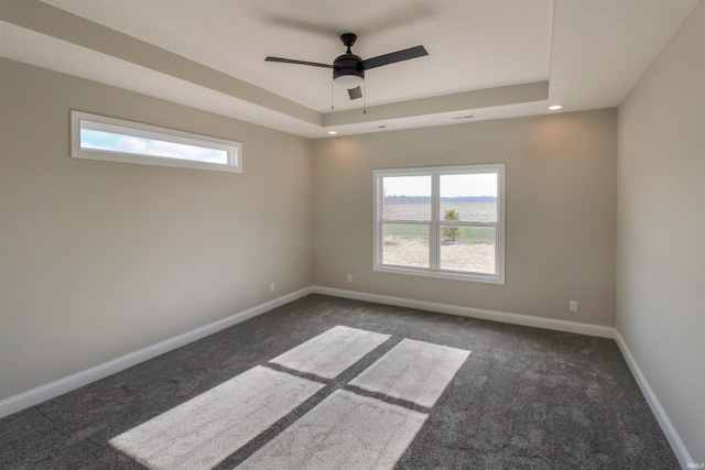 spare room featuring a tray ceiling, ceiling fan, and dark colored carpet