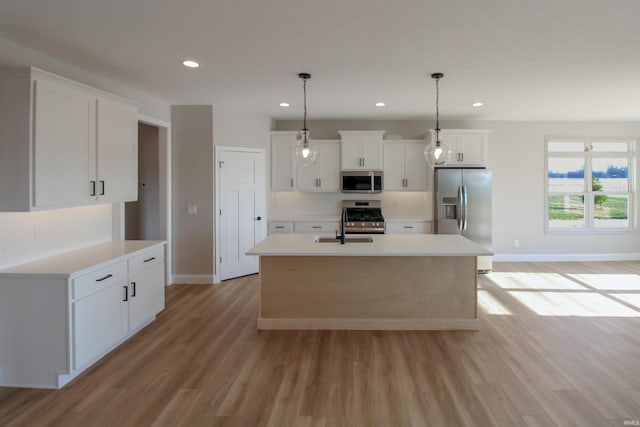 kitchen featuring appliances with stainless steel finishes, a kitchen island with sink, light hardwood / wood-style flooring, white cabinets, and hanging light fixtures