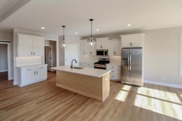 kitchen featuring hanging light fixtures, stainless steel appliances, an island with sink, white cabinets, and light wood-type flooring