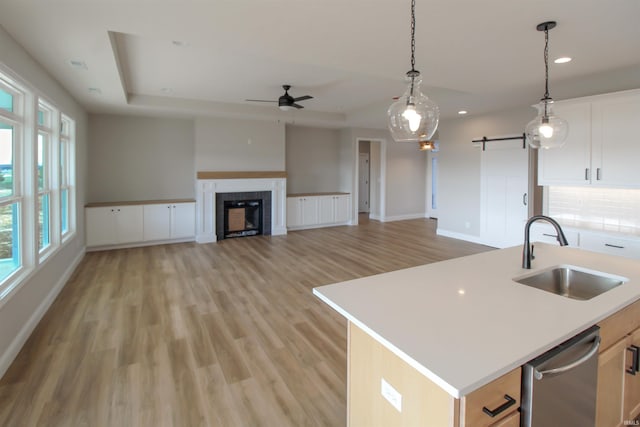 kitchen featuring stainless steel dishwasher, sink, a center island with sink, light hardwood / wood-style floors, and white cabinetry