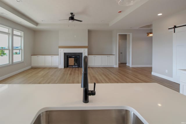 kitchen featuring a tray ceiling, ceiling fan, sink, and light wood-type flooring