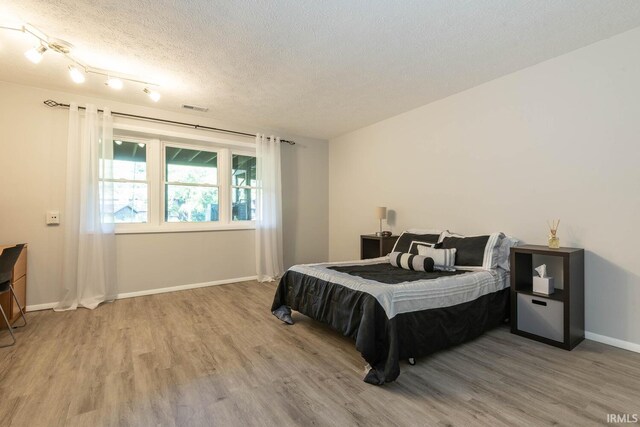 bedroom with a textured ceiling, hardwood / wood-style floors, and track lighting