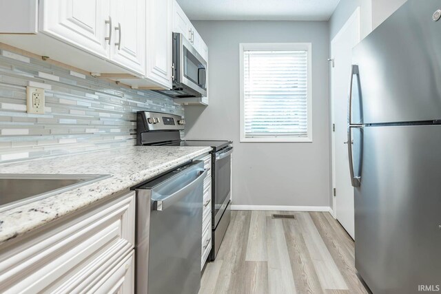 kitchen with appliances with stainless steel finishes, white cabinets, light stone counters, backsplash, and light wood-type flooring