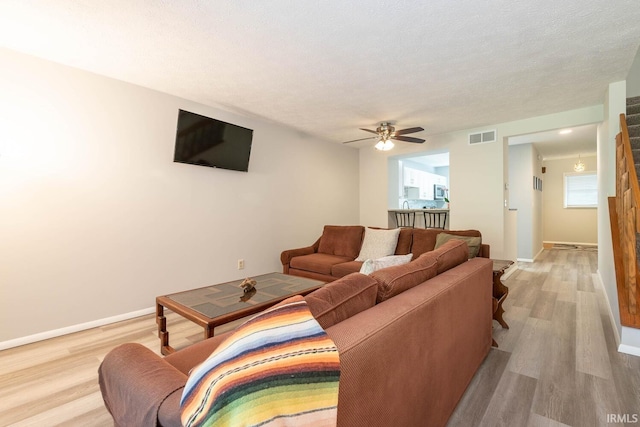 living room featuring a textured ceiling, light wood-type flooring, and ceiling fan