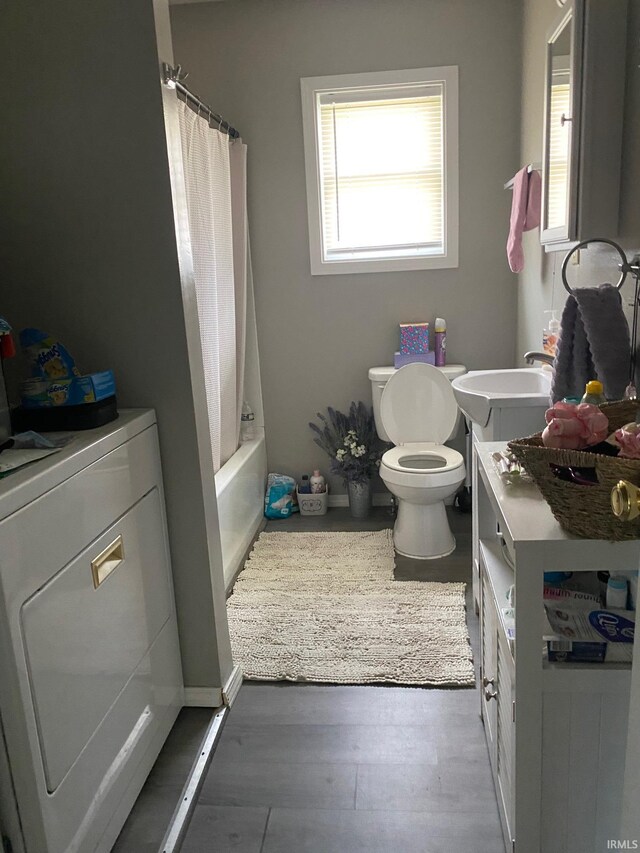 full bathroom featuring wood-type flooring, washer / dryer, sink, shower / tub combo, and toilet