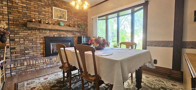 dining area with wood-type flooring, a notable chandelier, brick wall, and a fireplace