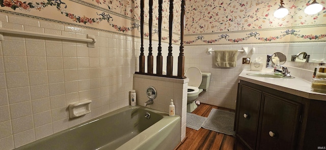 bathroom with a tub to relax in, toilet, wainscoting, tile walls, and wallpapered walls