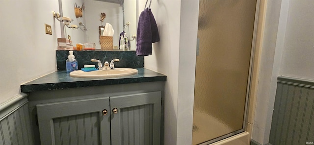 full bathroom featuring a decorative wall, wainscoting, vanity, decorative backsplash, and a stall shower