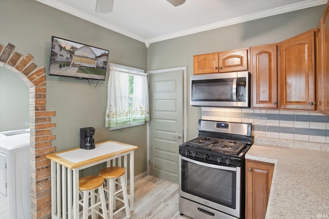 kitchen with backsplash, stainless steel appliances, light hardwood / wood-style floors, washer / dryer, and ornamental molding