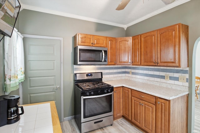 kitchen featuring ceiling fan, stainless steel appliances, crown molding, light hardwood / wood-style floors, and backsplash