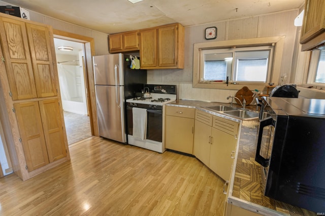 kitchen with white range with gas cooktop, sink, stainless steel fridge, and light wood-type flooring