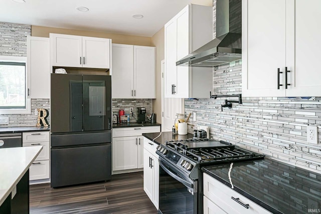 kitchen featuring gas stove, wall chimney range hood, black refrigerator, white cabinets, and decorative backsplash