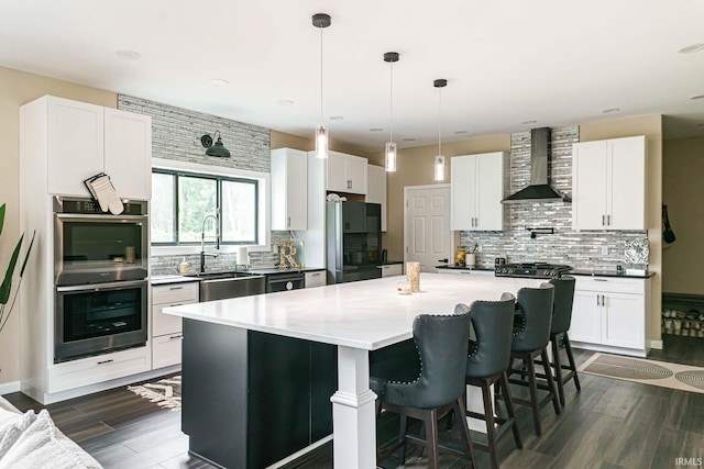 kitchen with wall chimney range hood, black refrigerator, decorative backsplash, a center island, and double oven