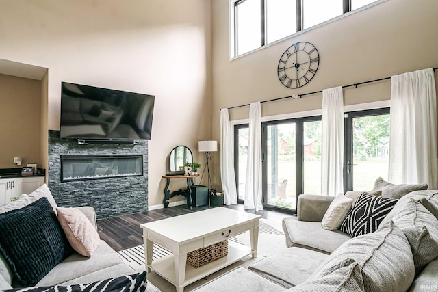 living room with hardwood / wood-style flooring, a stone fireplace, and a towering ceiling