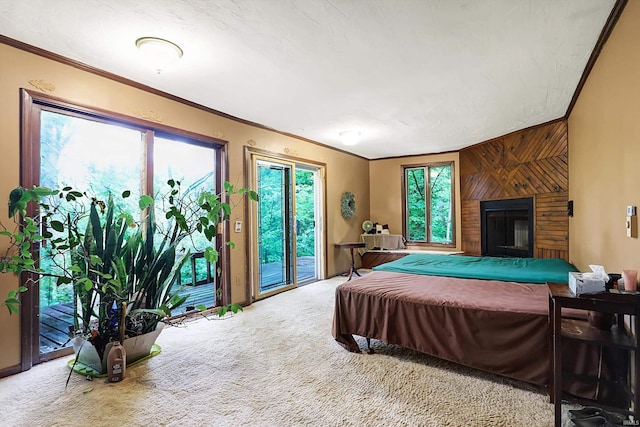 carpeted bedroom with access to exterior, a glass covered fireplace, wood walls, and ornamental molding