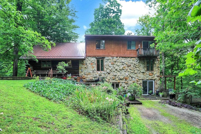 back of house featuring dirt driveway, a lawn, metal roof, fence, and stone siding