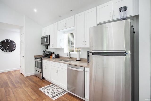 kitchen featuring sink, light stone counters, stainless steel appliances, hardwood / wood-style floors, and white cabinets