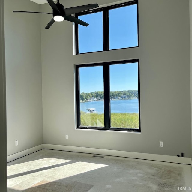 spare room featuring a towering ceiling, concrete floors, and a water view