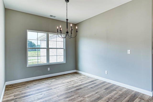 spare room with wood-type flooring and an inviting chandelier