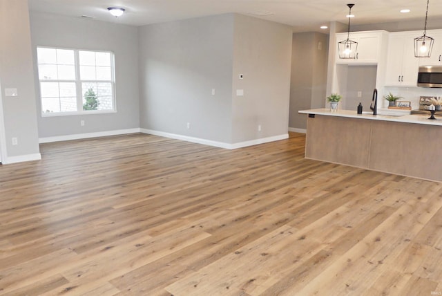 kitchen featuring pendant lighting, light hardwood / wood-style flooring, white cabinets, and appliances with stainless steel finishes