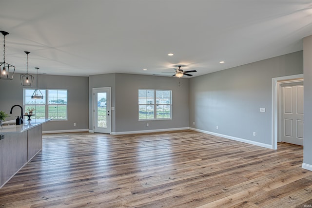 unfurnished living room with ceiling fan, sink, a healthy amount of sunlight, and light wood-type flooring