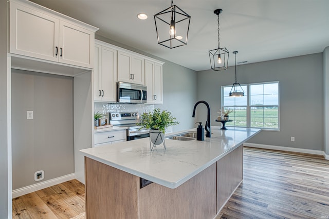 kitchen with appliances with stainless steel finishes, white cabinetry, sink, a kitchen island with sink, and light stone countertops